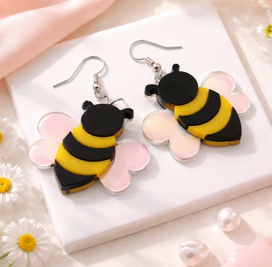 Bee-shaped acrylic dangle earrings with black and yellow bodies and iridescent wings on a soft neutral background