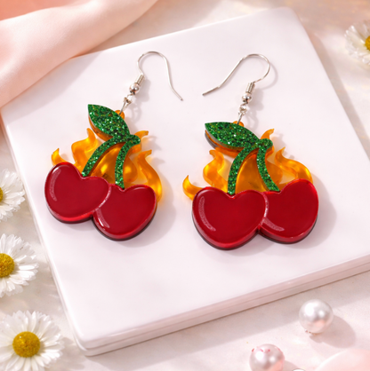 Cherry flame acrylic dangle earrings with red cherries, green glitter leaves, and translucent flame details on silver hooks