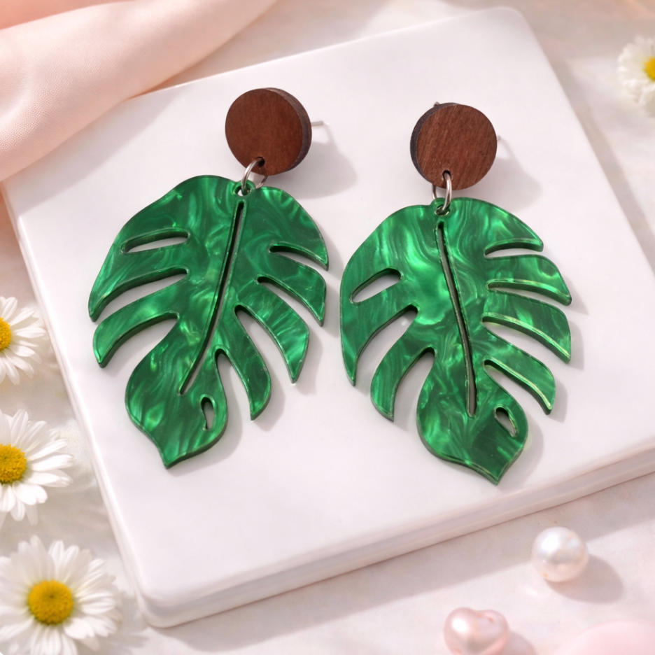 Green pearl acrylic monstera leaf dangle earrings with timber stud tops on a soft neutral background