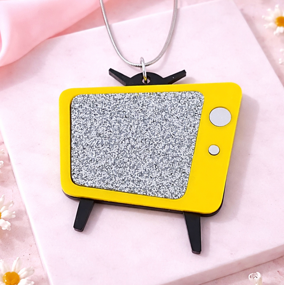 Yellow retro TV necklace with glitter screen displayed on pink tile background