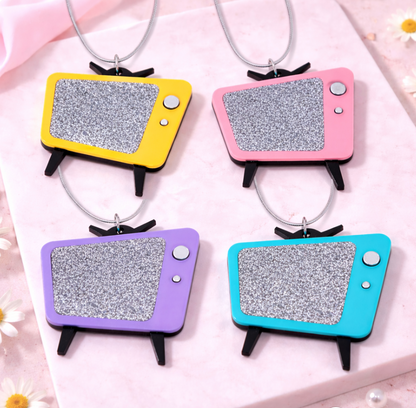 Four retro TV necklaces in yellow, pink, purple and turquoise on pink tile background